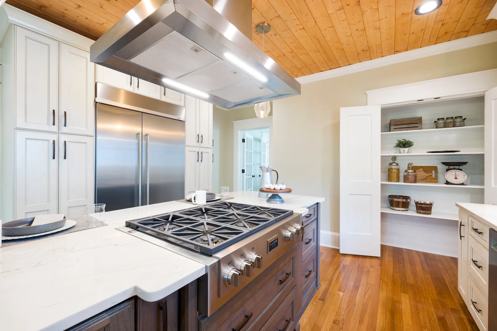 Emhætte i stål hænger over et gaskomfur i et lyst køkken med træloft